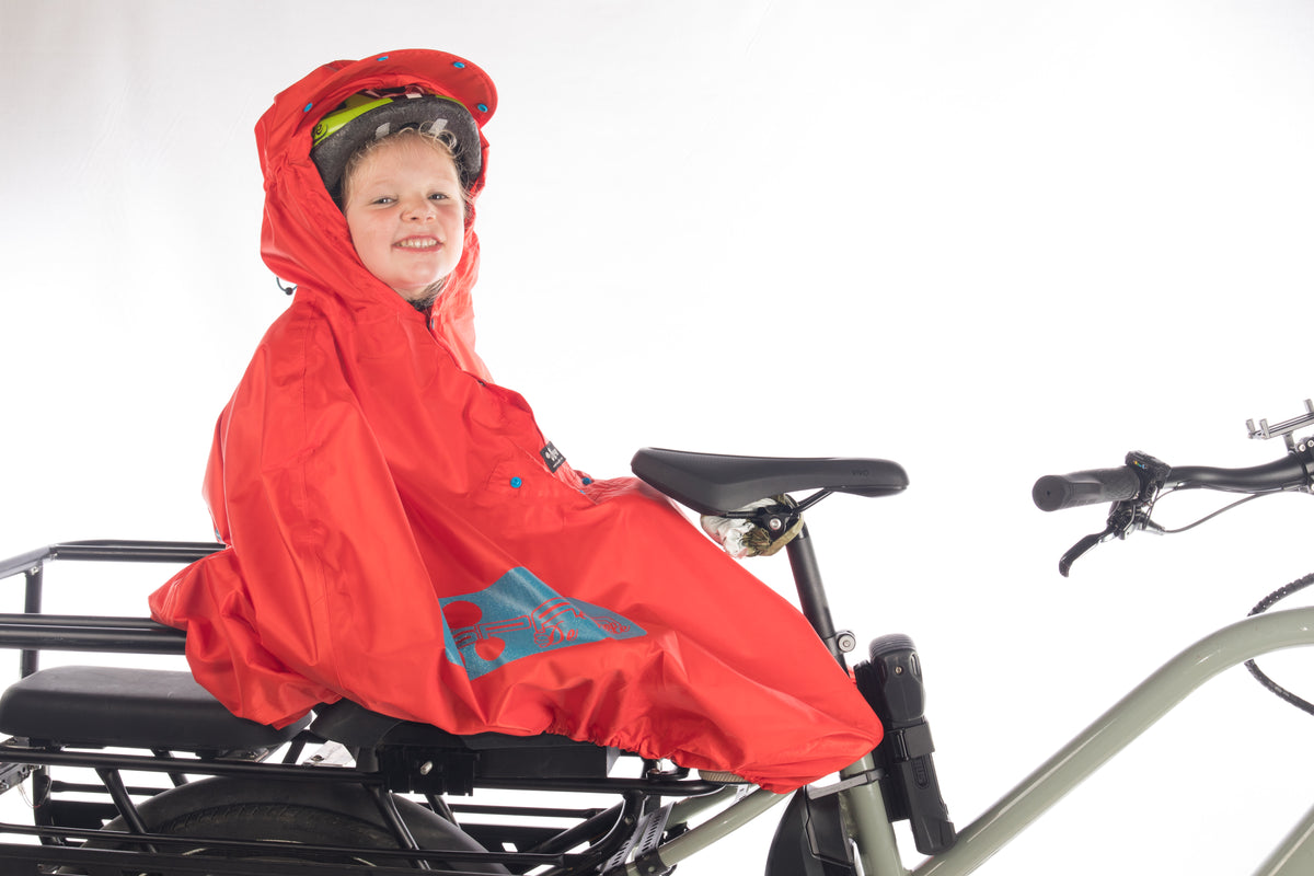 SPAD De Ville FULAP Junior la cape de pluie vélo protection intérale et multiusages pour les enfants de 1 à 12 ans rouge haute visibilité motifs rétro-réfléchissants bleu vue de profil sur longtail peugeot douze cycle avec un monkey bar